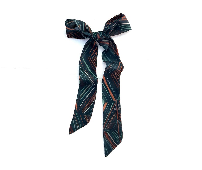 May include: A dark green and orange patterned hair tie with a bow.