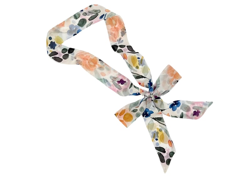 May include: A floral patterned scarf with a bow. The scarf features a watercolor design with peach, blue, yellow, and purple flowers on a white background. The scarf is tied in a bow at the center.