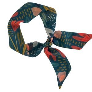 May include: A teal blue patterned scarf with red, pink, and yellow floral designs. The scarf is tied in a knot.