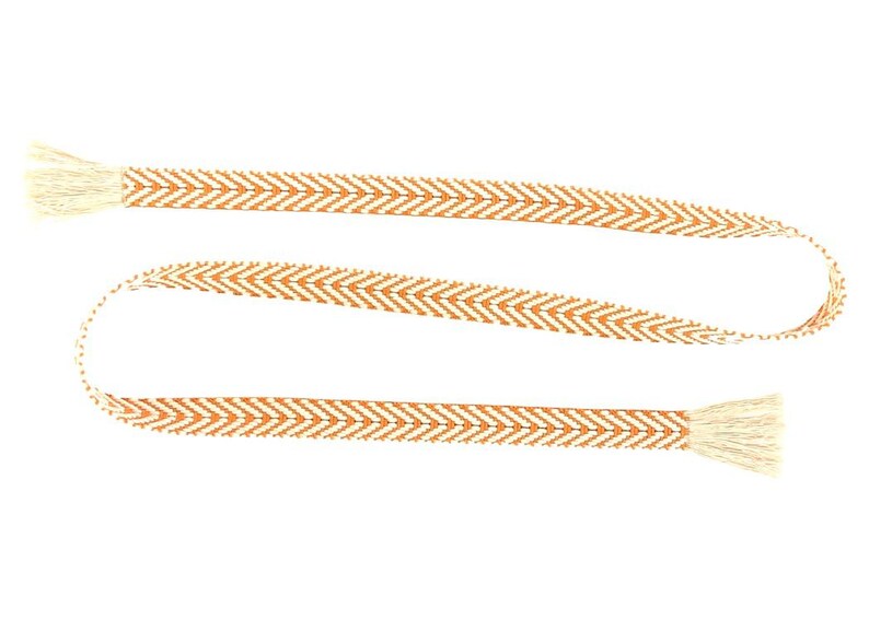 May include: A long, thin, orange and white woven ribbon with tassels on each end. The ribbon has a chevron pattern.