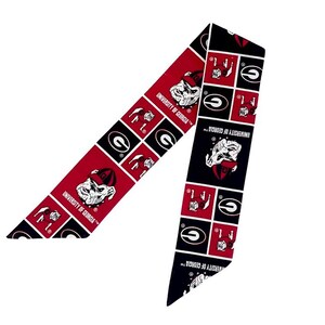 Puede incluir: Una cinta de tela larga y estrecha con un patr&oacute;n repetitivo de cuadrados rojos y negros. El dise&ntilde;o incluye el logotipo de la mascota bulldog de la University of Georgia y el texto University of Georgia impreso en blanco sobre fondos rojos y negros.
