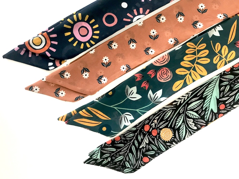 May include: Four fabric headbands with different floral patterns. The headbands are in shades of pink, orange, yellow, green, blue, and black.