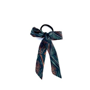 May include: A green, brown and white patterned hair tie with a bow.