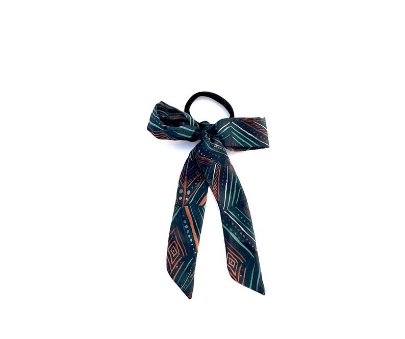 May include: A green, brown and white patterned hair tie with a bow.