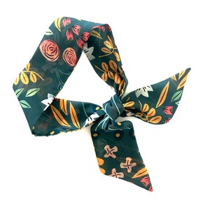 May include: A teal blue fabric hair scarf with a floral pattern in shades of pink, yellow, and green. The scarf is tied in a bow.