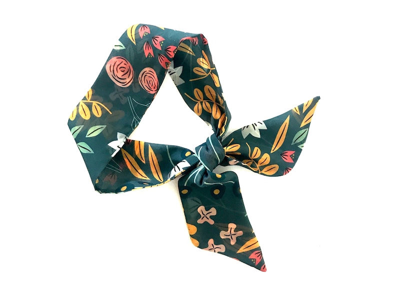 May include: A teal blue fabric hair scarf with a floral pattern in shades of pink, yellow, and green. The scarf is tied in a bow.
