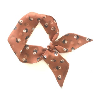 May include: A brown floral patterned hair scarf tied in a bow.