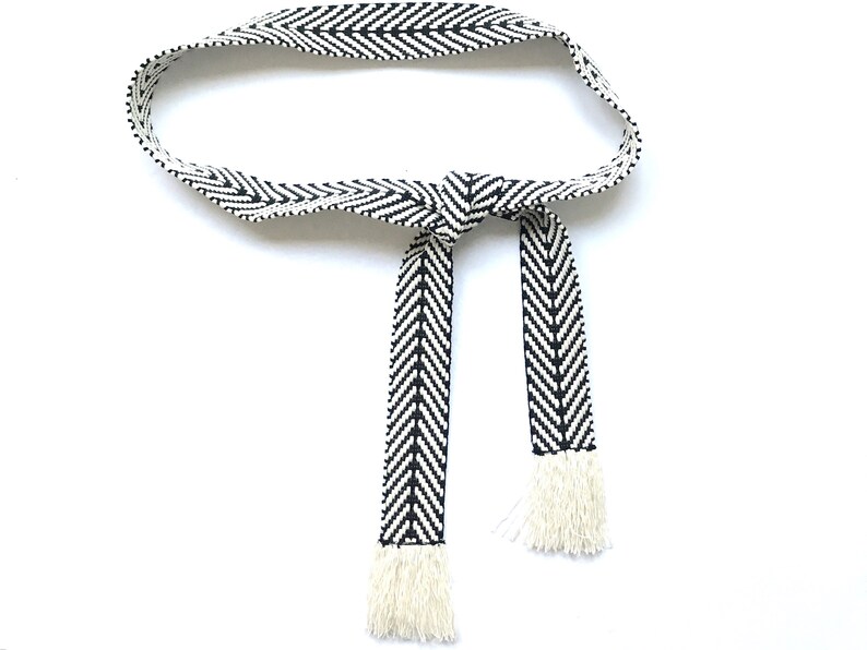 May include: A black and white chevron patterned belt with white fringe tassels.
