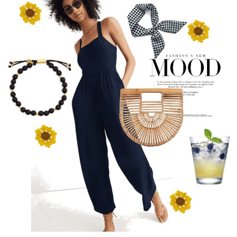 May include: A navy blue jumpsuit, a black beaded bracelet, a brown woven bag, a black and white checkered headband, a glass of yellow lemonade with blueberries, and sunflowers.