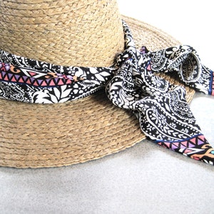 May include: A straw hat with a black and white paisley patterned ribbon tied around it. The ribbon has pink, blue, and orange accents.