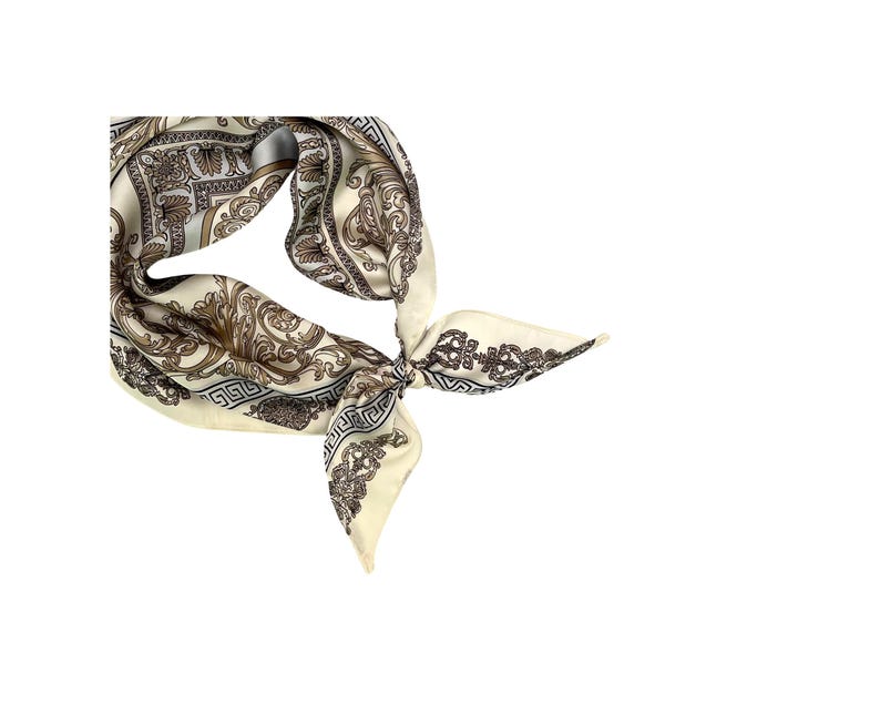May include: Ivory-colored silk scarf with a detailed baroque pattern in shades of brown and black. The scarf is knotted, showcasing its intricate design and elegant style. A classic accessory.