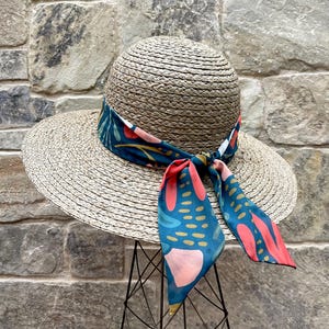 May include: A wide-brimmed straw hat with a teal, pink and red patterned ribbon tied around the crown.