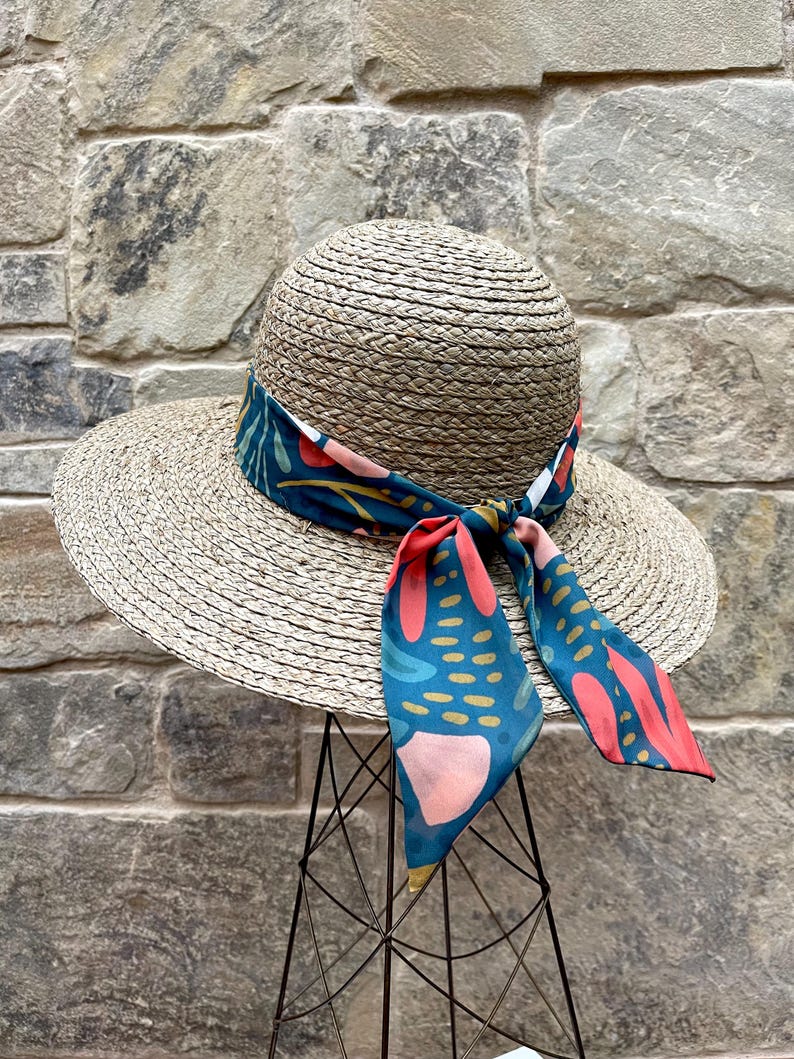 May include: A wide-brimmed straw hat with a teal, pink and red patterned ribbon tied around the crown.