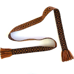 May include: A brown and black woven belt with tassels on each end. The belt has a geometric pattern.