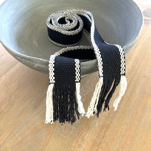 May include: Black and white woven trim with fringe. The trim is coiled in a bowl.