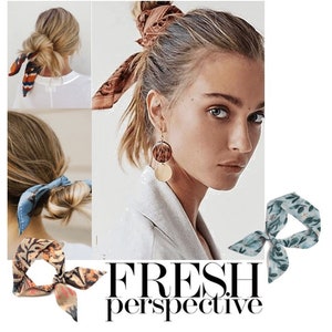 May include: Four different floral patterned silk scarves tied in a bow. The scarves are in shades of blue, green, orange, and brown. The scarves are shown tied around a woman's hair in a bun.