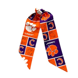 May include: A Clemson Tigers hair scarf in orange and purple. The scarf features the Clemson paw print and the letter "C" in a repeating pattern. The word "CLEMSON" is printed on the scarf.