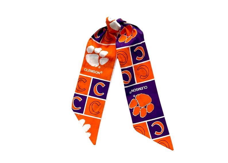May include: A Clemson Tigers hair scarf in orange and purple. The scarf features the Clemson paw print and the letter "C" in a repeating pattern. The word "CLEMSON" is printed on the scarf.