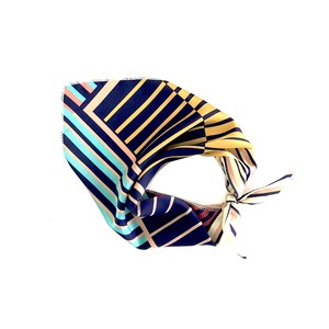 May include: A navy blue, yellow, pink, and turquoise patterned bandana with a geometric design. The bandana is tied in a knot.