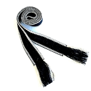 Pu&ograve; includere: Una cintura intrecciata in bianco e nero con frange. La cintura &egrave; realizzata in un tessuto spesso e strutturato e presenta un design geometrico semplice.