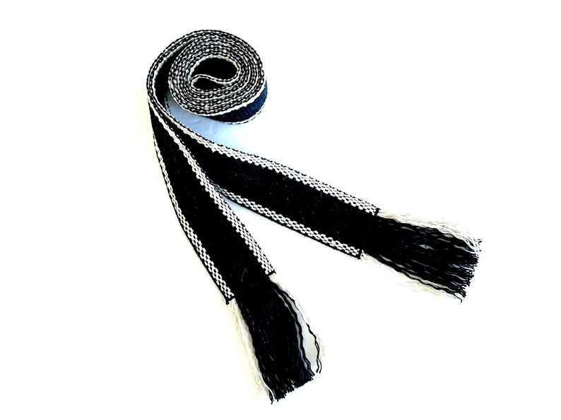 Pu&ograve; includere: Una cintura intrecciata in bianco e nero con frange. La cintura &egrave; realizzata in un tessuto spesso e strutturato e presenta un design geometrico semplice.