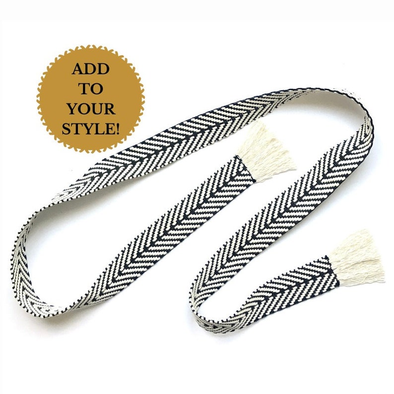 May include: Black and white woven belt with fringe ends. The belt is approximately 1.5 inches wide and has a chevron pattern. The text "ADD TO YOUR STYLE!" is on a gold circle.