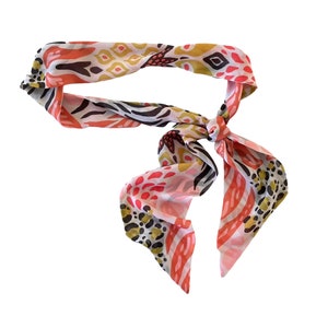 May include: A pink, white, and gold patterned scarf with a knotted design.