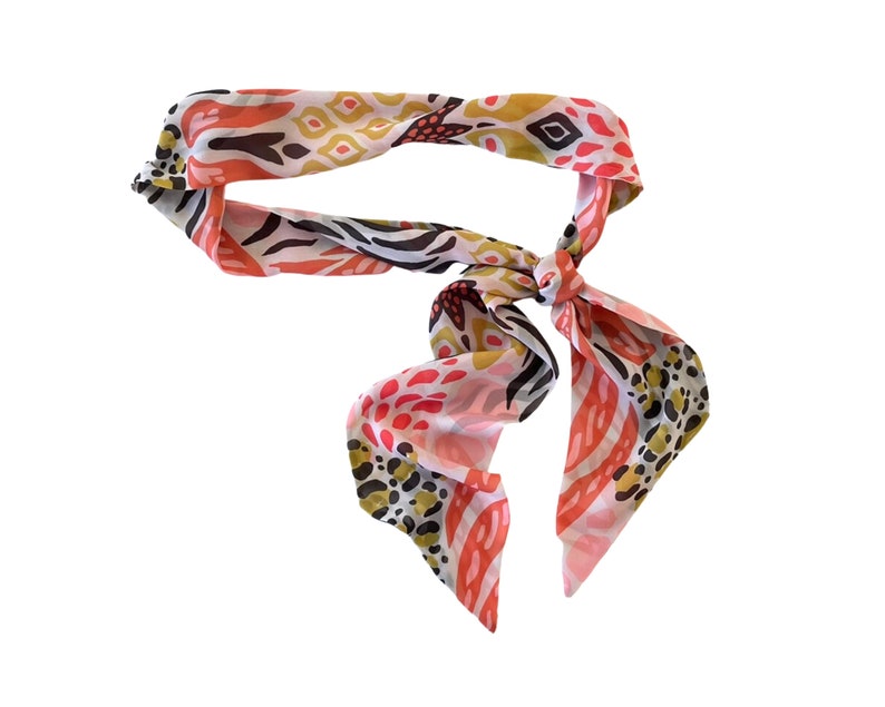 May include: A pink, white, and gold patterned scarf with a knotted design.