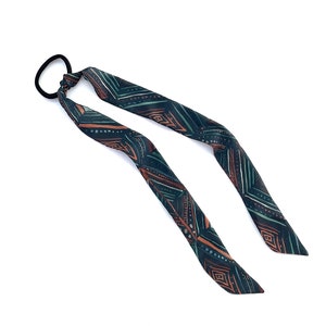 May include: A black hair tie with a long, patterned fabric tail. The fabric is dark green with a geometric pattern in shades of orange and brown.