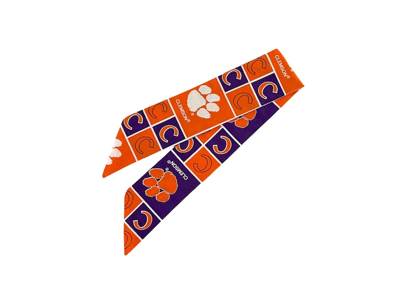 May include: Two fabric headbands in orange and purple, featuring a repeating pattern of the Clemson paw print and the letter "C" inside a square. The word "CLEMSON" is printed on the headband.
