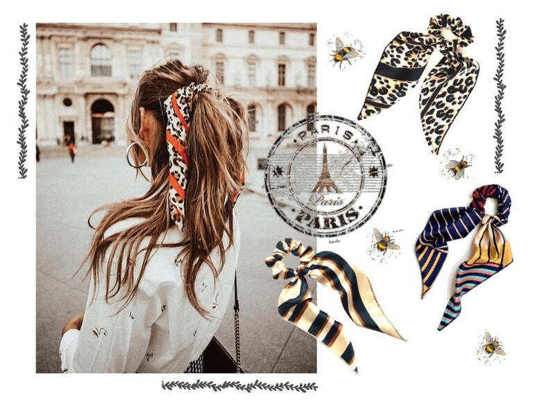 May include: Three different patterned hair scrunchies. The scrunchies are made of fabric and have a bow on top. The scrunchies are in a leopard print, a striped pattern, and a blue and yellow pattern. The image also includes a woman with brown hair wearing a leopard print scrunchie in her hair.