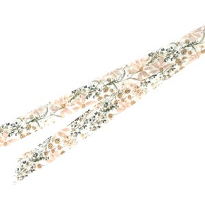 以下が含まれることがあります： ピンクの花、緑の葉、金色のアクセントが施された花柄の白い布のリボンです。