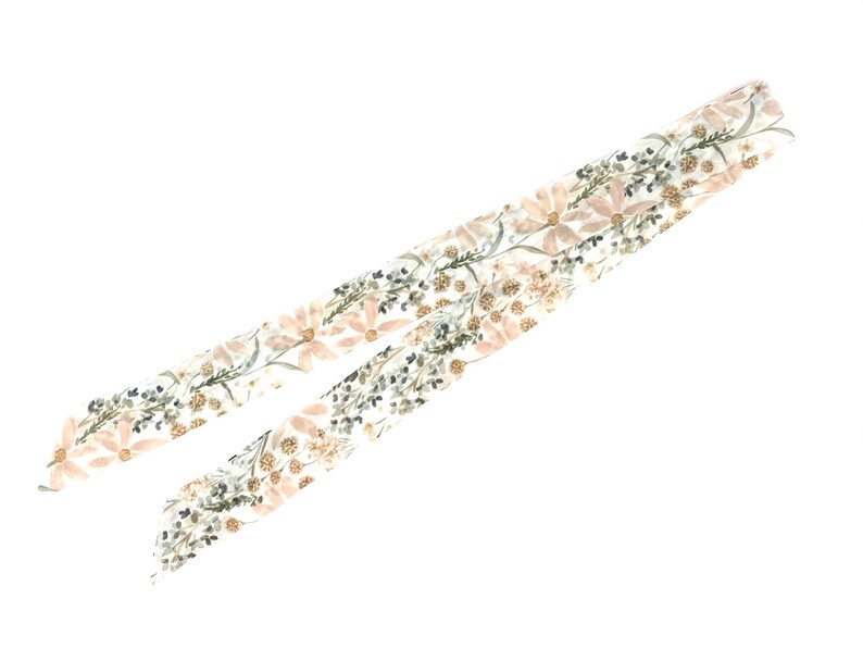 以下が含まれることがあります： ピンクの花、緑の葉、金色のアクセントが施された花柄の白い布のリボンです。
