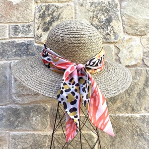 May include: A wide-brimmed straw hat with a pink, black, and gold patterned scarf tied around the crown.