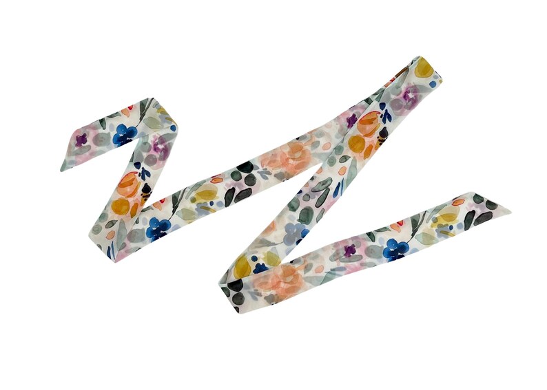 May include: A floral patterned ribbon in a watercolor style. The ribbon features a white background with colorful flowers in shades of blue, orange, yellow, and purple. The ribbon is folded in a zig-zag pattern.