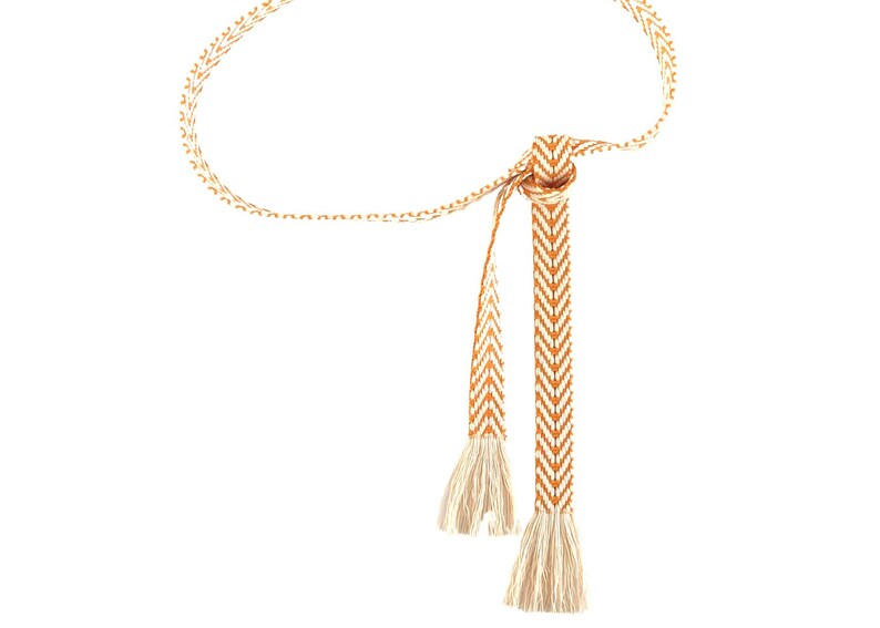 May include: A woven orange and white belt with tassels. The belt is made of a chevron pattern.