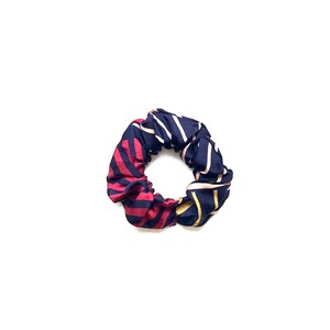 May include: A navy blue and red striped scrunchie with gold accents.