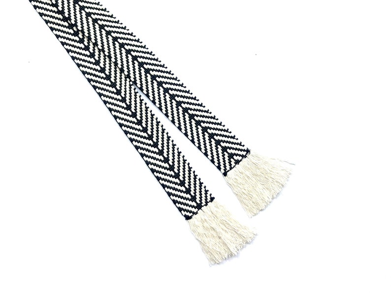 May include: Black and white chevron patterned ribbon with white fringe on both ends.