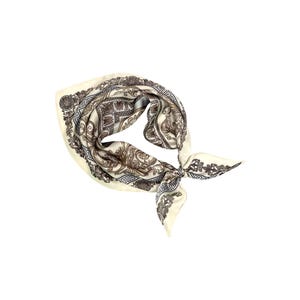 May include: Ivory-colored silk scarf with a detailed brown and gray pattern. The scarf is knotted and features an ornate design with floral and geometric elements. The scarf is a square shape.