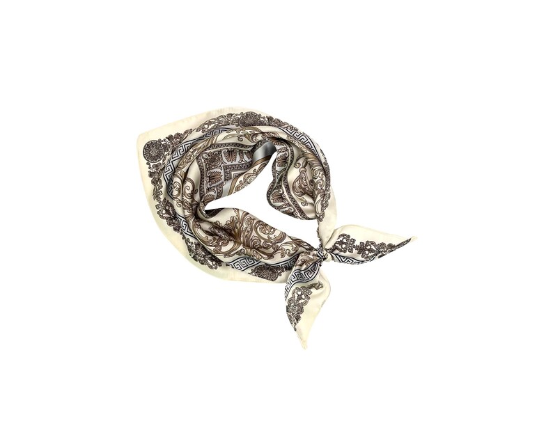 May include: Ivory-colored silk scarf with a detailed brown and gray pattern. The scarf is knotted and features an ornate design with floral and geometric elements. The scarf is a square shape.