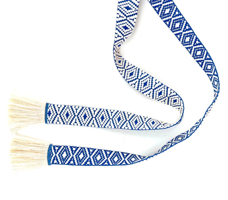 May include: A blue and white patterned ribbon with fringe tassels on each end. The ribbon is woven with a geometric diamond pattern.