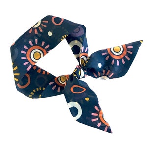 May include: A navy blue silk scarf with a colorful abstract pattern of circles and sunbursts. The scarf is tied in a knot.