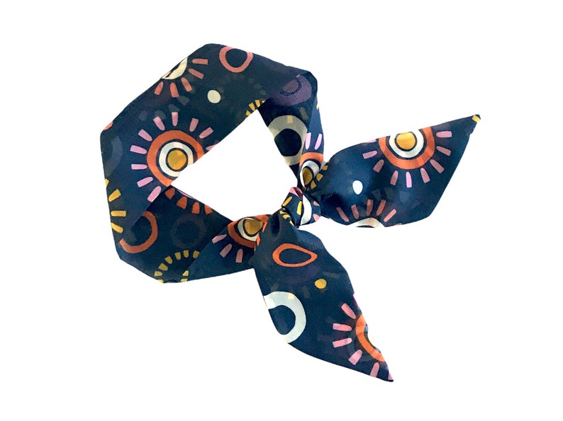 May include: A navy blue silk scarf with a colorful abstract pattern of circles and sunbursts. The scarf is tied in a knot.