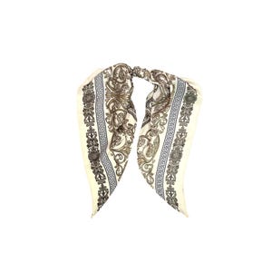 May include: Ivory-colored silk scarf with a detailed baroque pattern in black and gold. The scarf features a repeating Greek key border design and ornate floral and scroll motifs, creating a luxurious accessory.