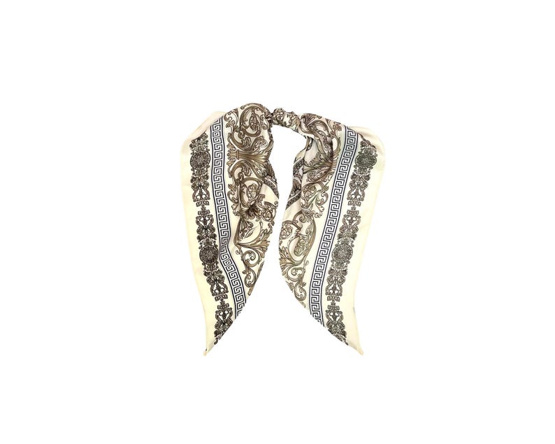 May include: Ivory-colored silk scarf with a detailed baroque pattern in black and gold. The scarf features a repeating Greek key border design and ornate floral and scroll motifs, creating a luxurious accessory.