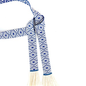May include: A blue and white woven belt with tassels. The belt has a geometric pattern and is tied in a knot.