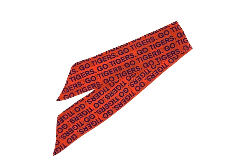 May include: Orange and navy blue head scarf with the text "GO TIGERS" repeated across the fabric. The scarf is tied in a knot, with the ends pointing towards the bottom left and top right corners.