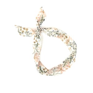 以下が含まれることがあります： ピンクと緑の花が咲いた花柄の白いヘッドバンド。ヘッドバンドは頭の上で結ばれています。
