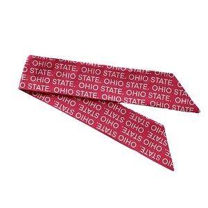 Pode incluir: Um len&ccedil;o de cetim vermelho com a inscri&ccedil;&atilde;o repetida "OHIO STATE" em branco. O len&ccedil;o est&aacute; dobrado e inclinado, com as extremidades apontando para baixo &agrave; direita. O fundo &eacute; branco liso.