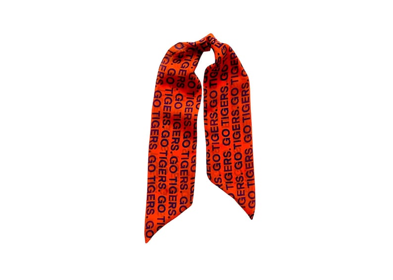 May include: Orange fabric hair scarf with the text "GO TIGERS" in black repeated vertically. The scarf is tied at the top, with two long, pointed ends hanging down.